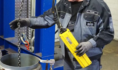 Mitarbeiter in GKD-Arbeitskleidung bedient einen gelben Steuergriff mit Hebekette.